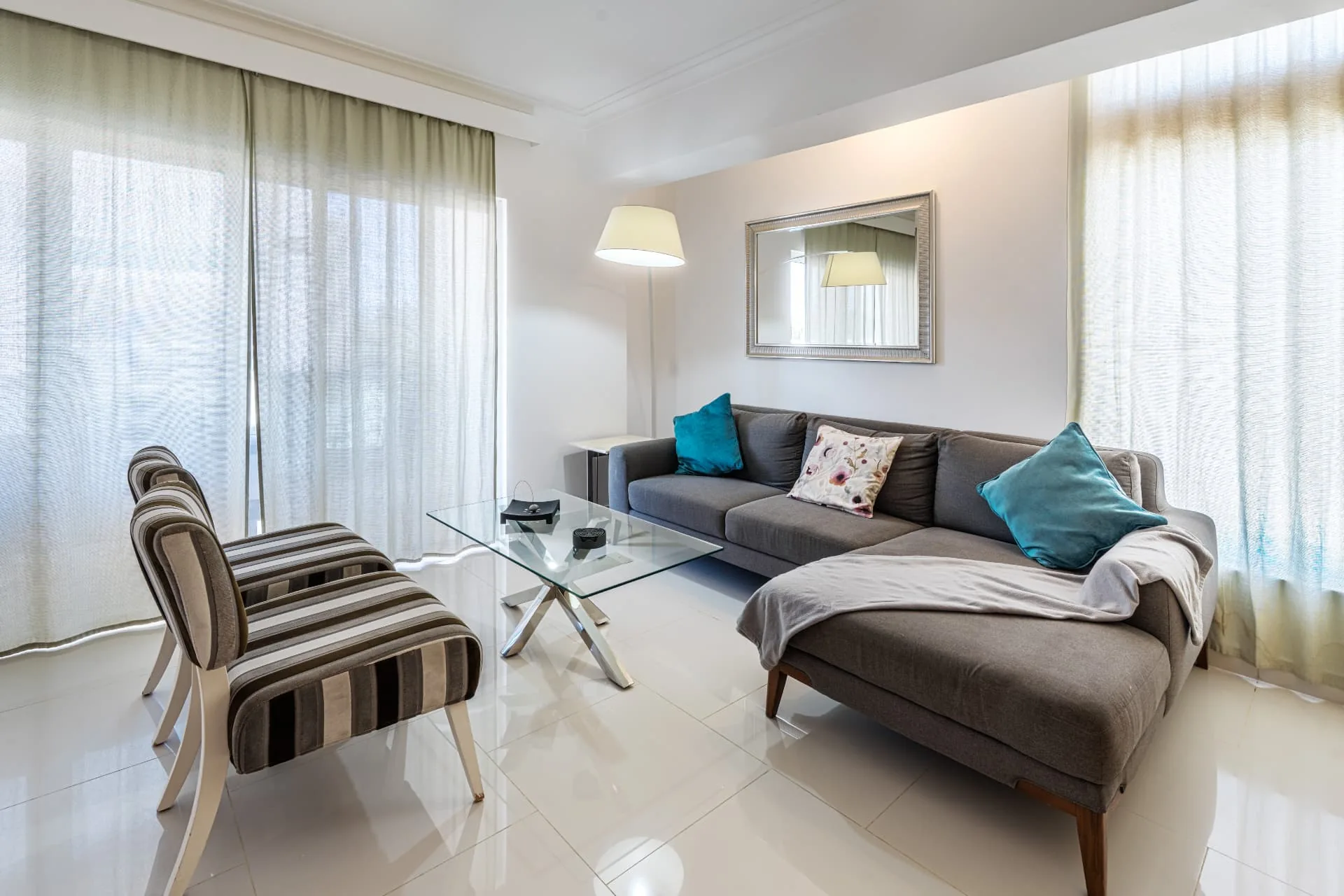 Bright condominium living room with grey sectional sofa, teal cushions and sheer floor-to-ceiling curtains