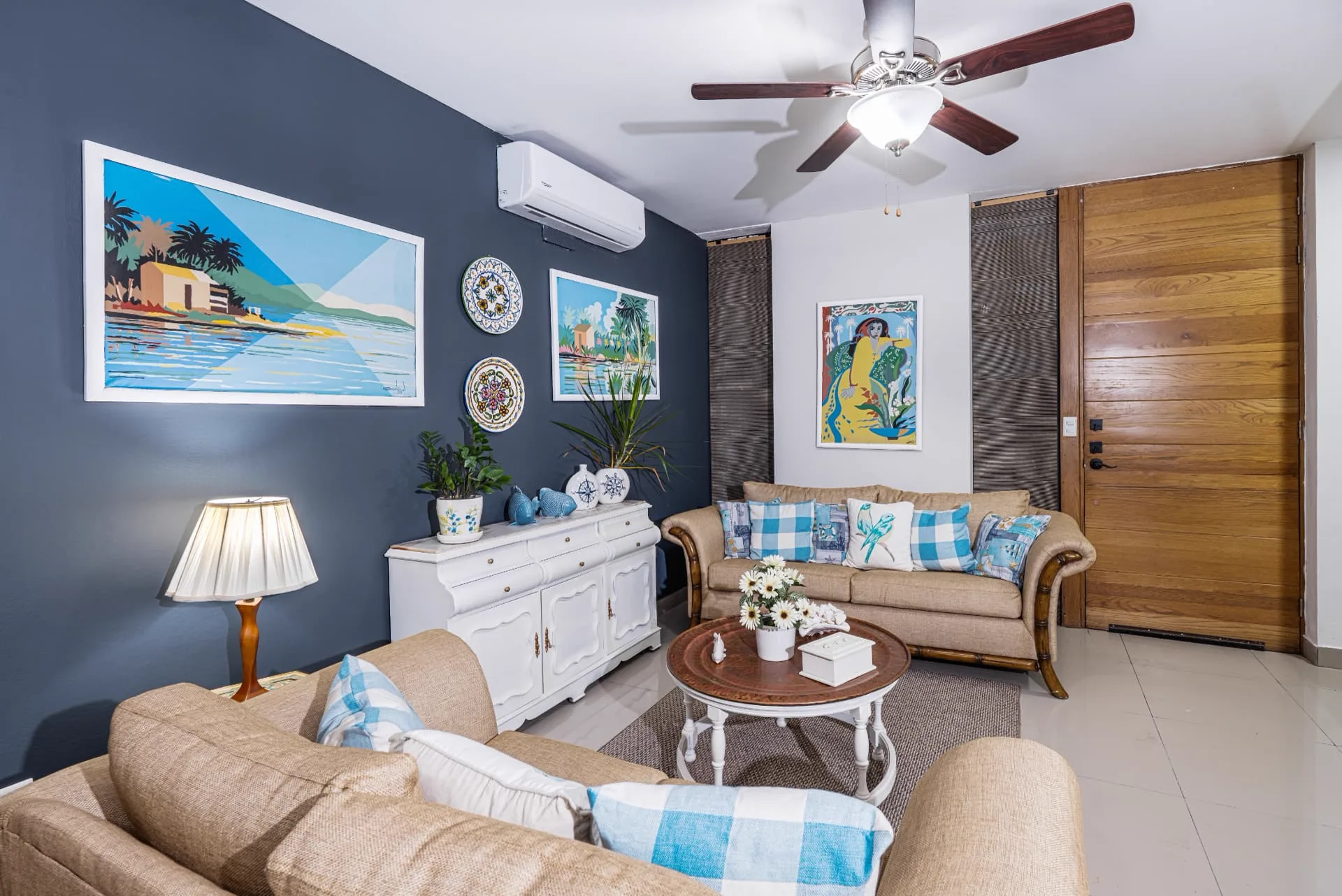 Living room at White Sand with navy feature wall, tropical artwork, linen sofas and blue gingham cushions