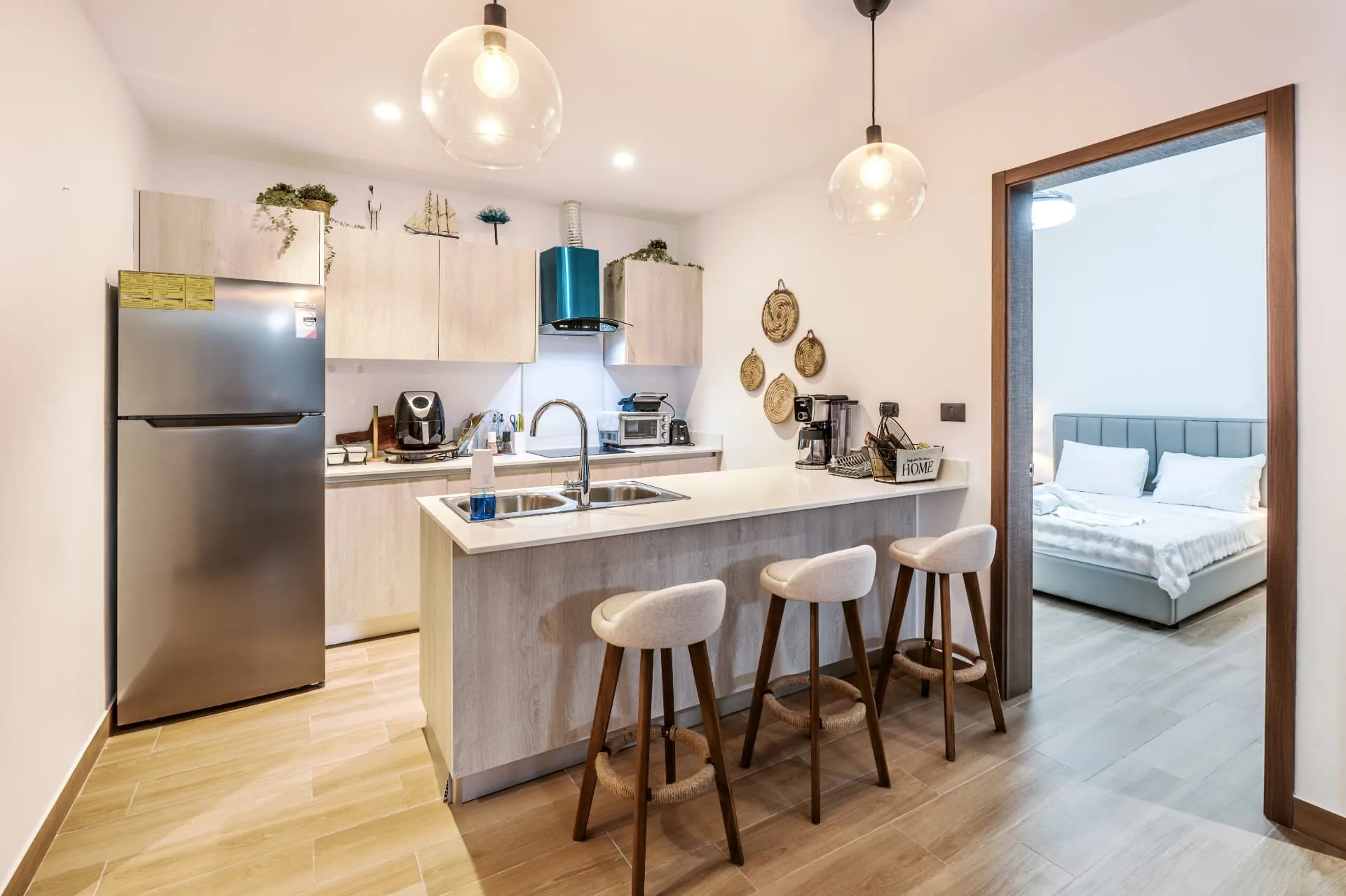 Kitchen with light timber cabinetry, teal range hood, breakfast bar and three upholstered stools