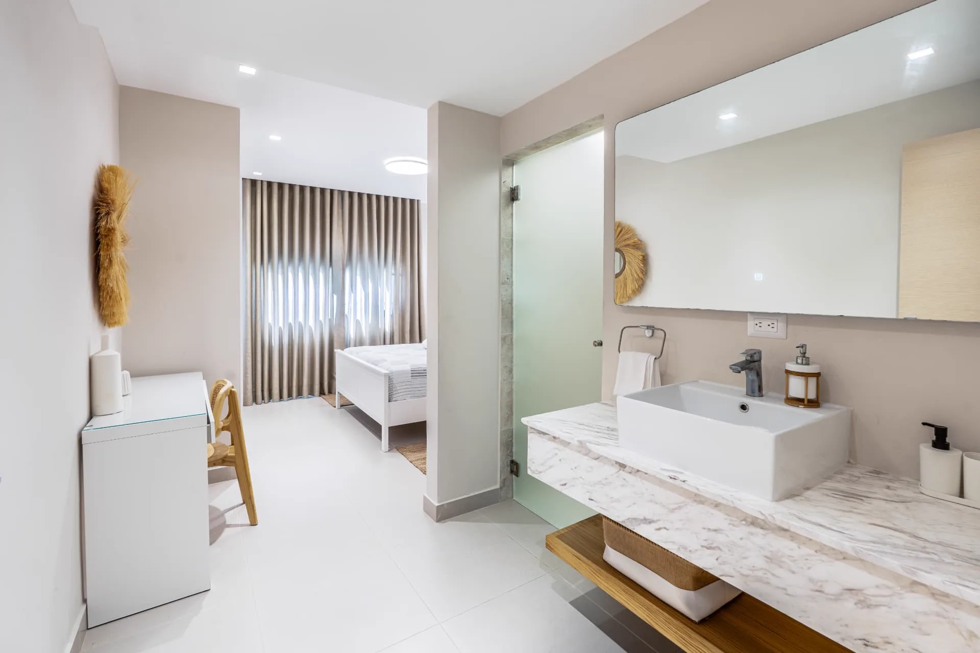 Marble vessel-sink vanity with a wide backlit mirror opening onto the bedroom beyond