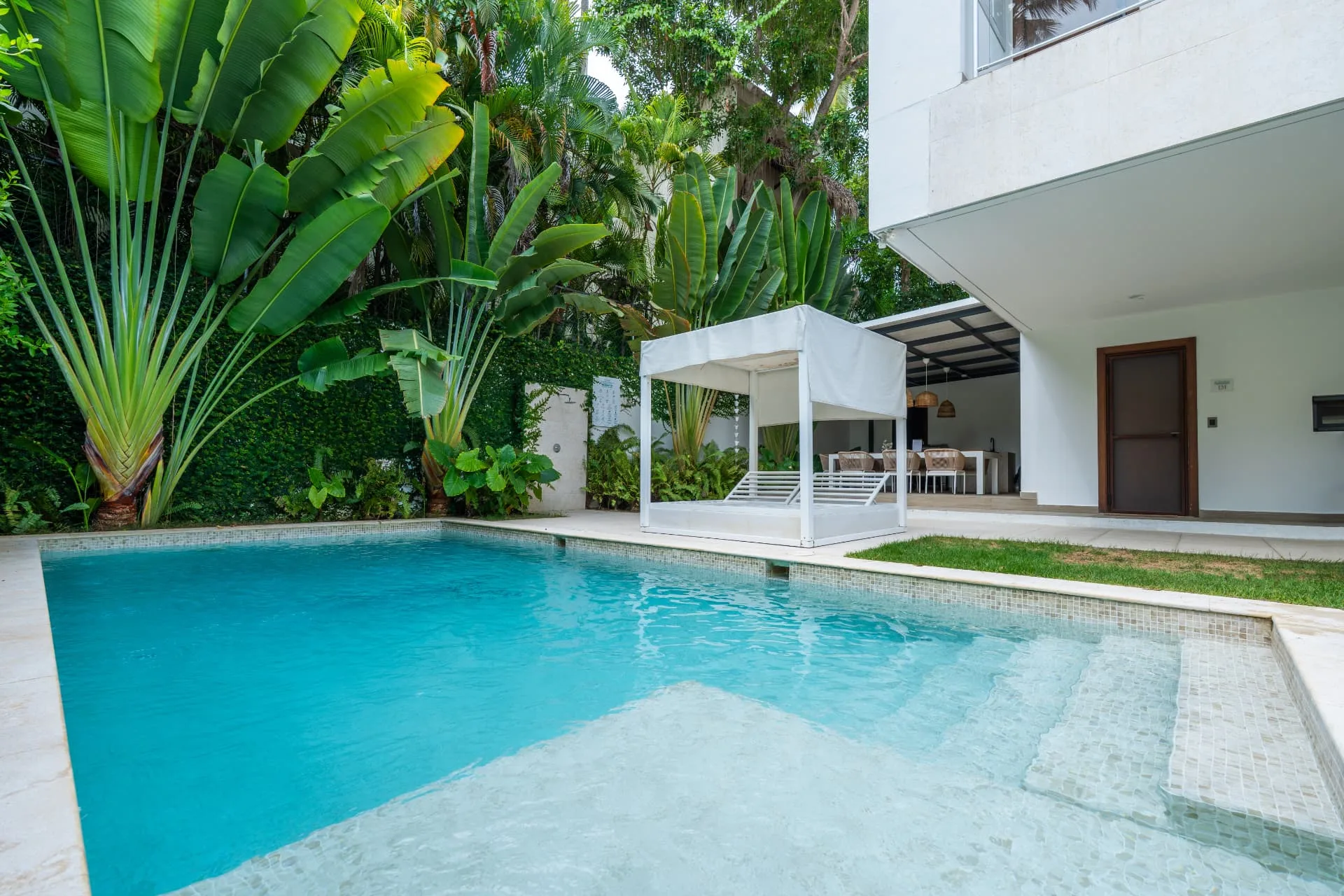 Turquoise swimming pool with a white canopy day bed, tropical planting and shaded outdoor lounge