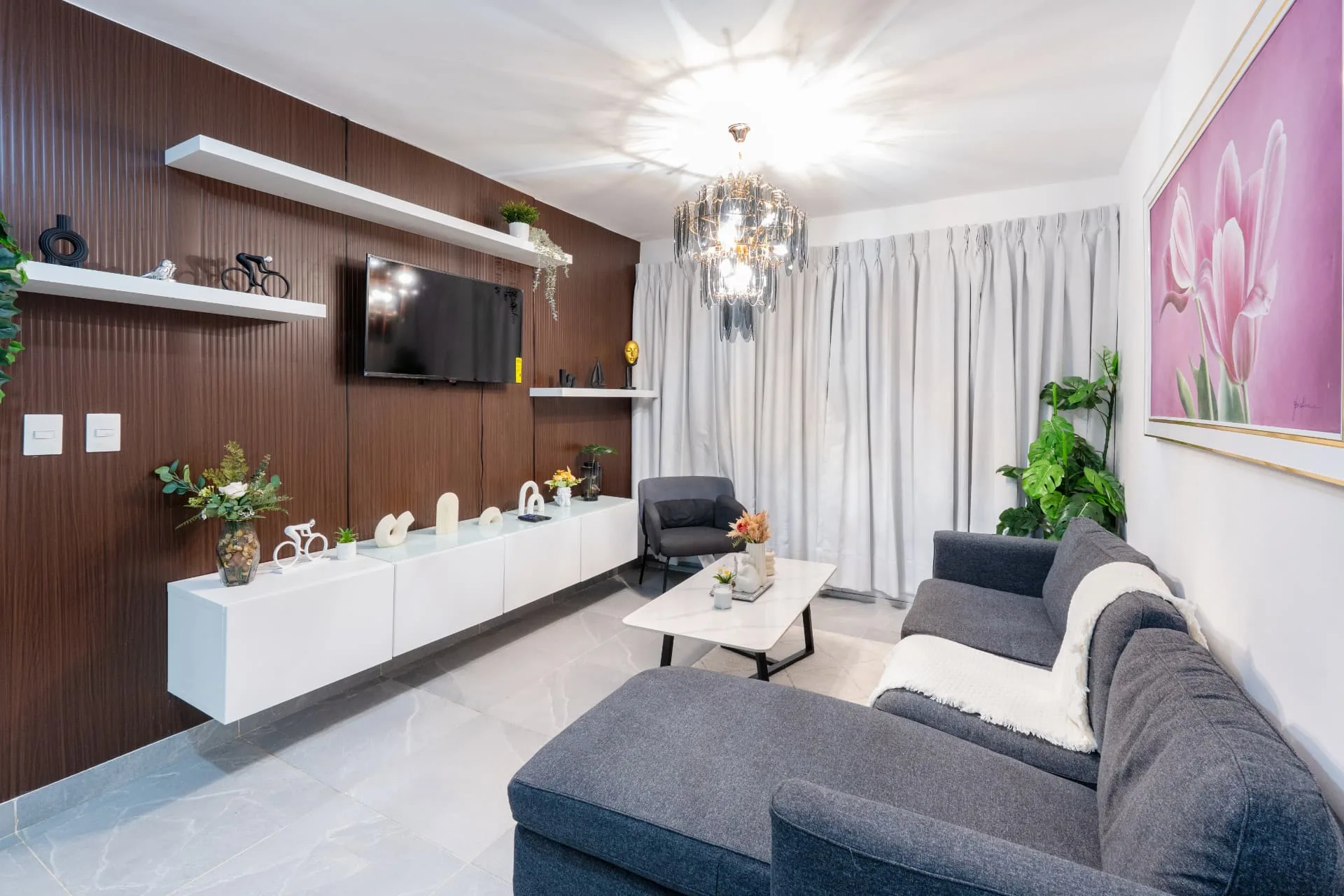 Styled apartment living room with walnut media wall, chandelier and grey sectional sofa