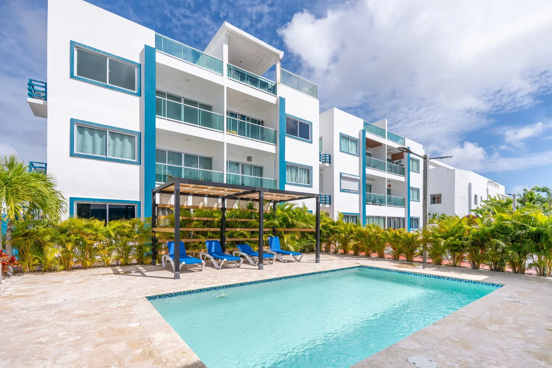 White and blue apartment building with pergola, loungers and swimming pool