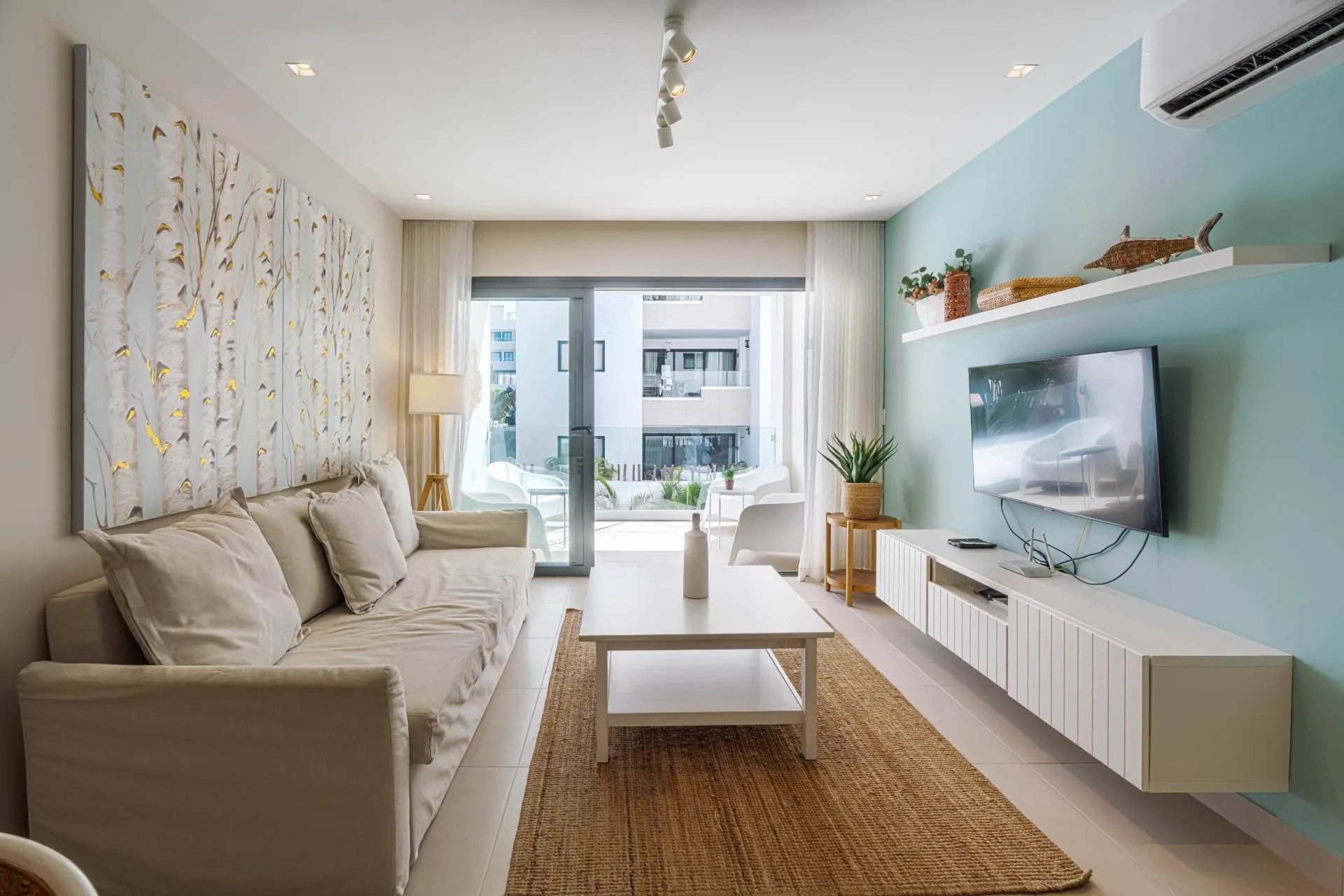 Living room with linen sofa and birch-forest canvas opening onto the furnished terrace through sliding glass doors