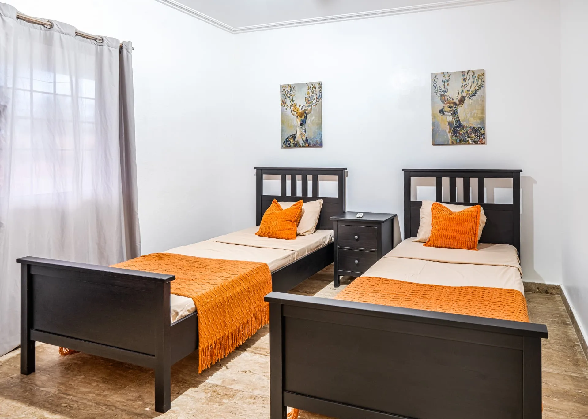 Twin bedroom with dark wood beds, orange throws and pillows and a pair of framed deer prints