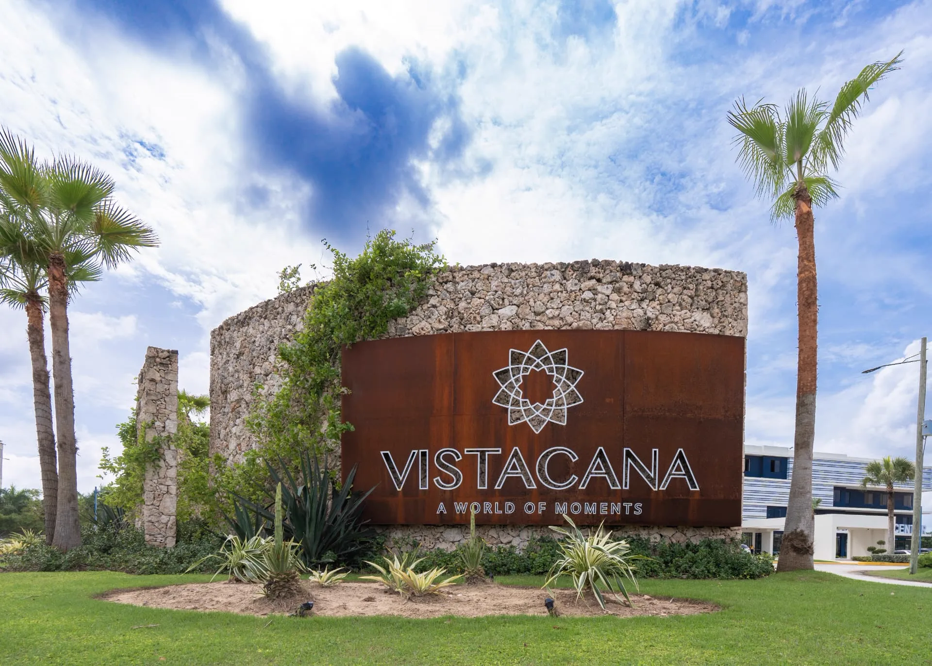 Coral stone and weathered steel Vista Cana entrance monument framed by palms