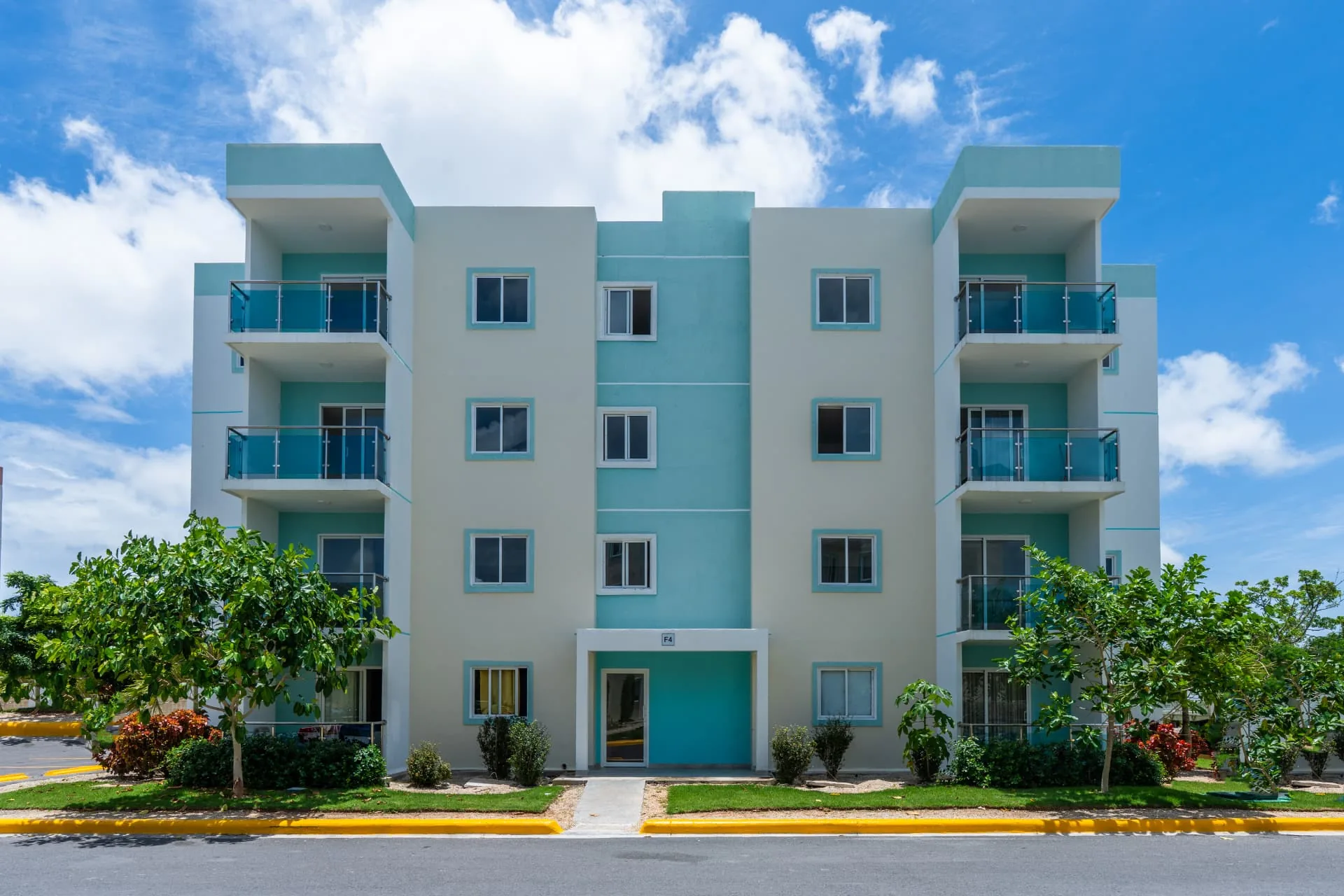 Symmetrical four-storey condominium facade with turquoise accents, glass balconies and landscaped frontage
