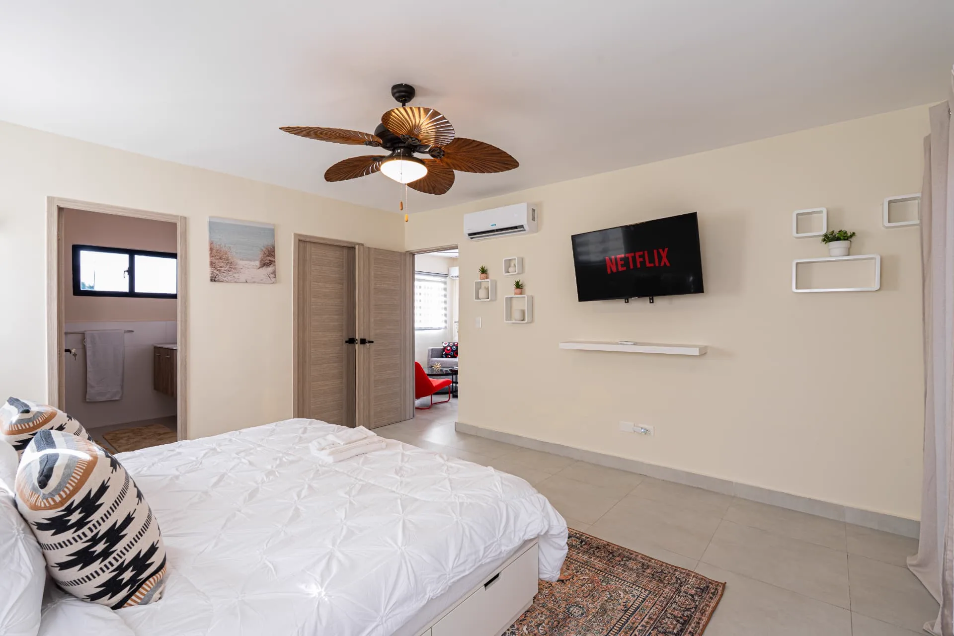 Primary bedroom looking toward the wall-mounted television, floating shelves and the en-suite bathroom door