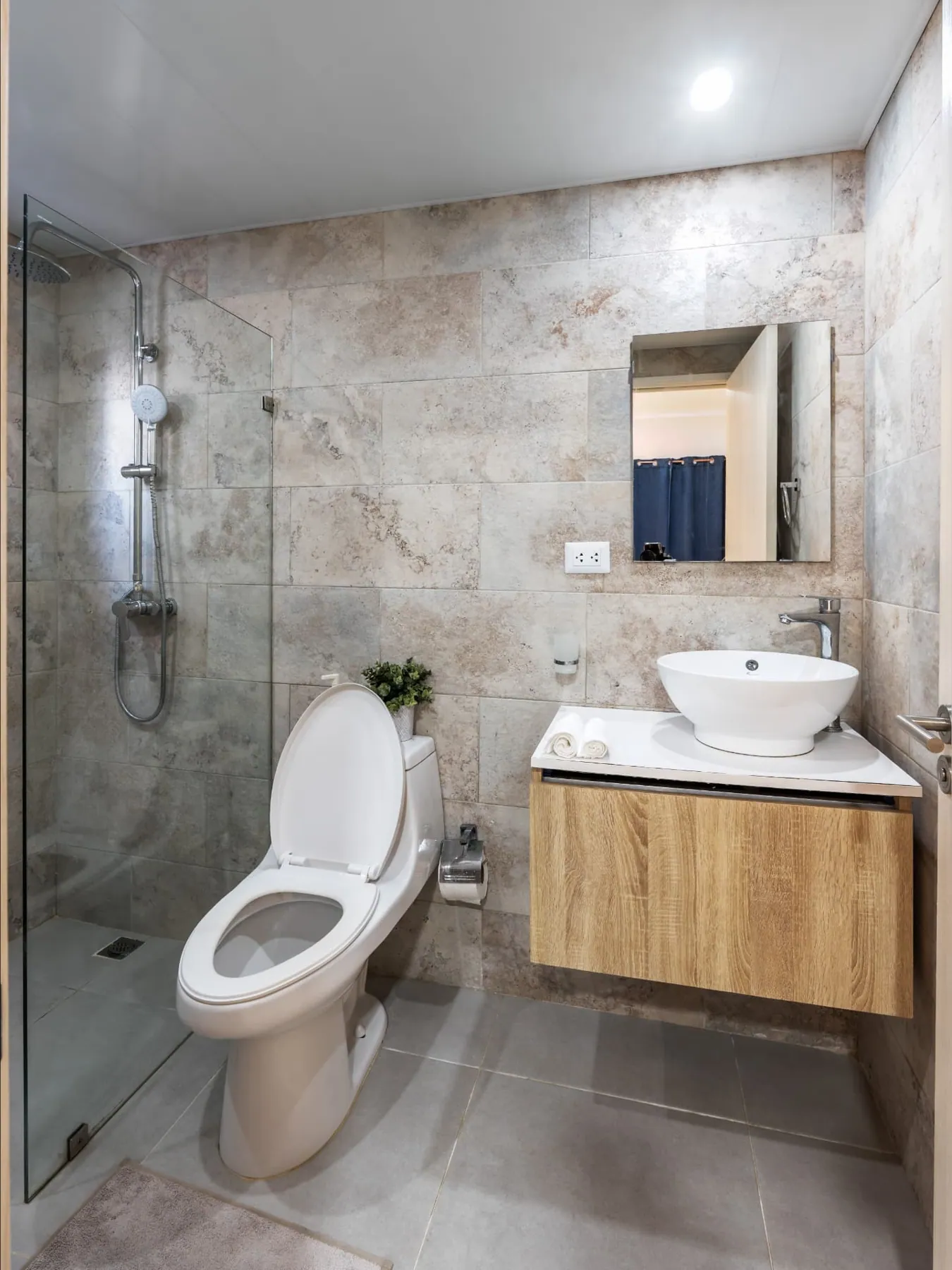 Travertine-tiled bathroom with glass walk-in shower, vessel sink and floating timber vanity