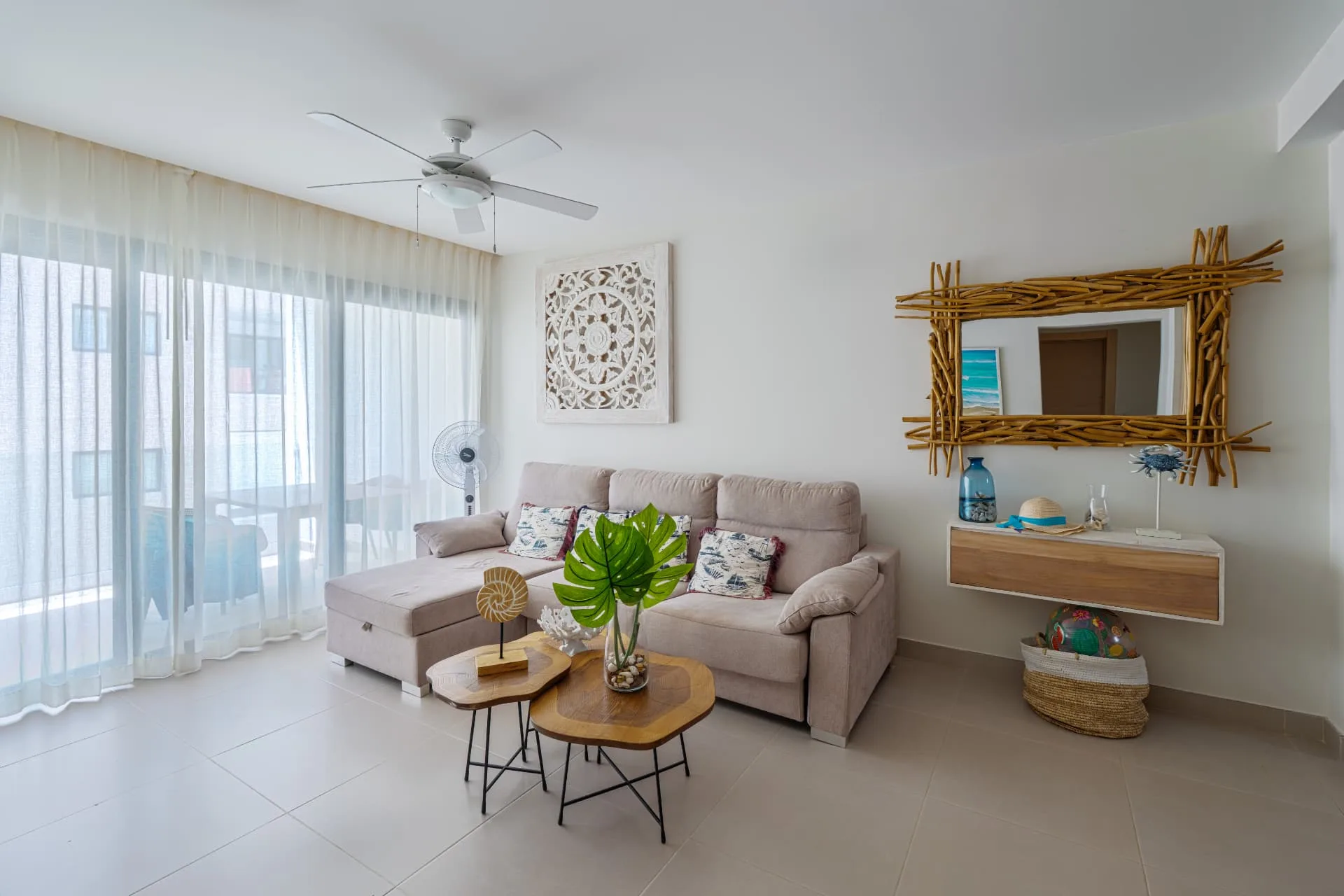 Bright coastal living room with pale sectional sofa, driftwood mirror and sheer curtains onto the balcony