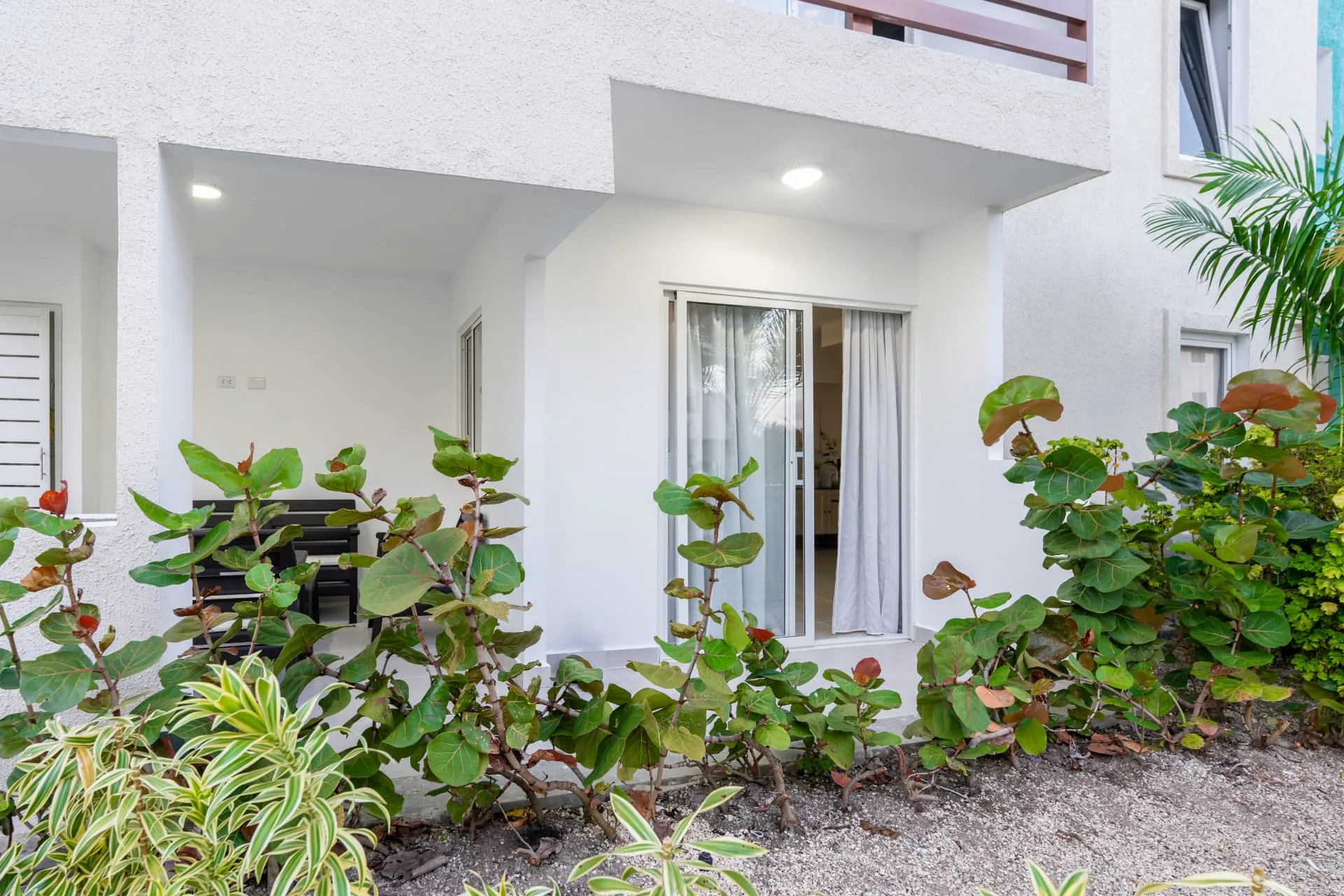 Ground-floor unit entrance with sliding glass doors, covered terrace and sea-grape landscaping