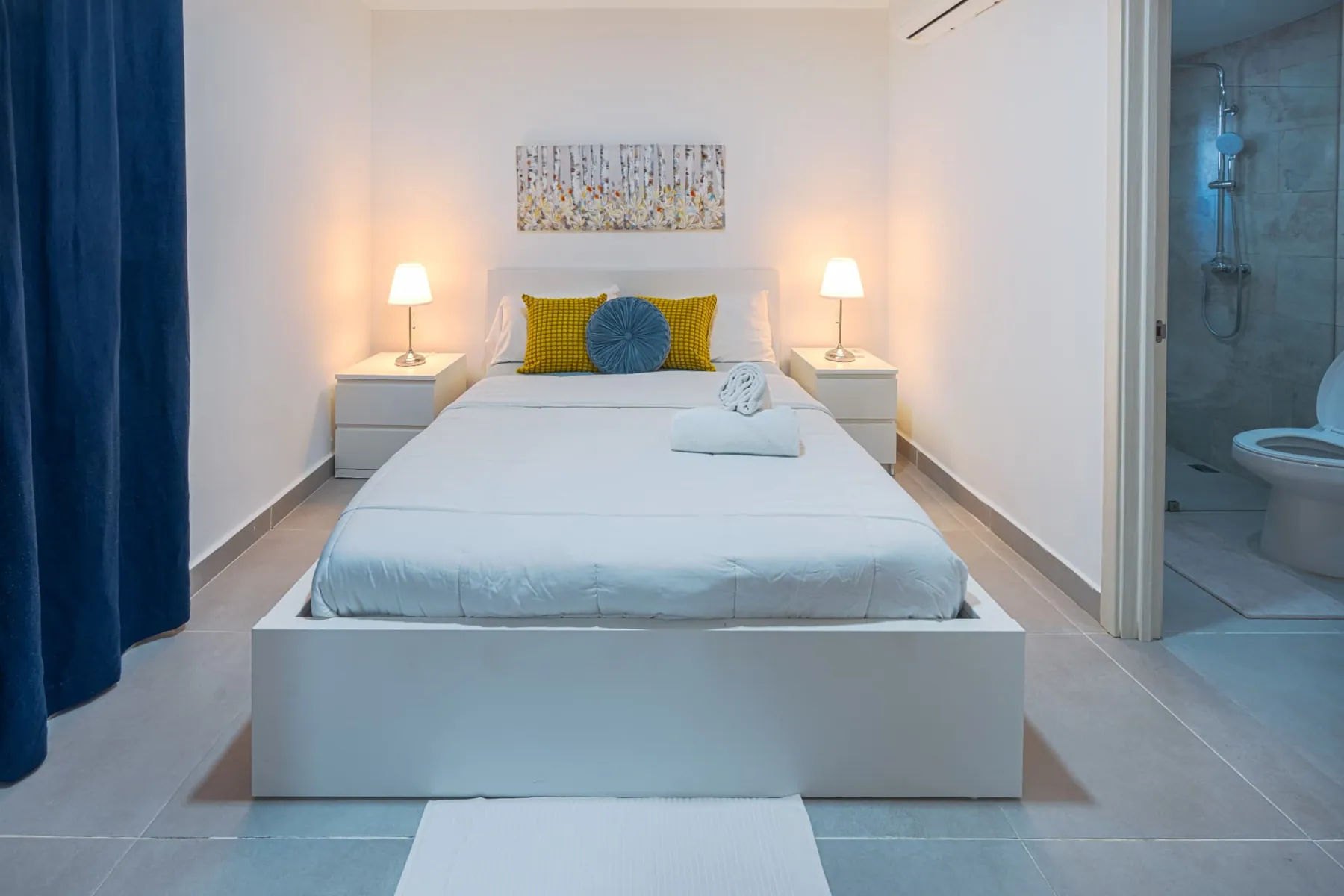 Primary bedroom with queen bed, twin lamps, botanical artwork and en-suite bathroom beyond