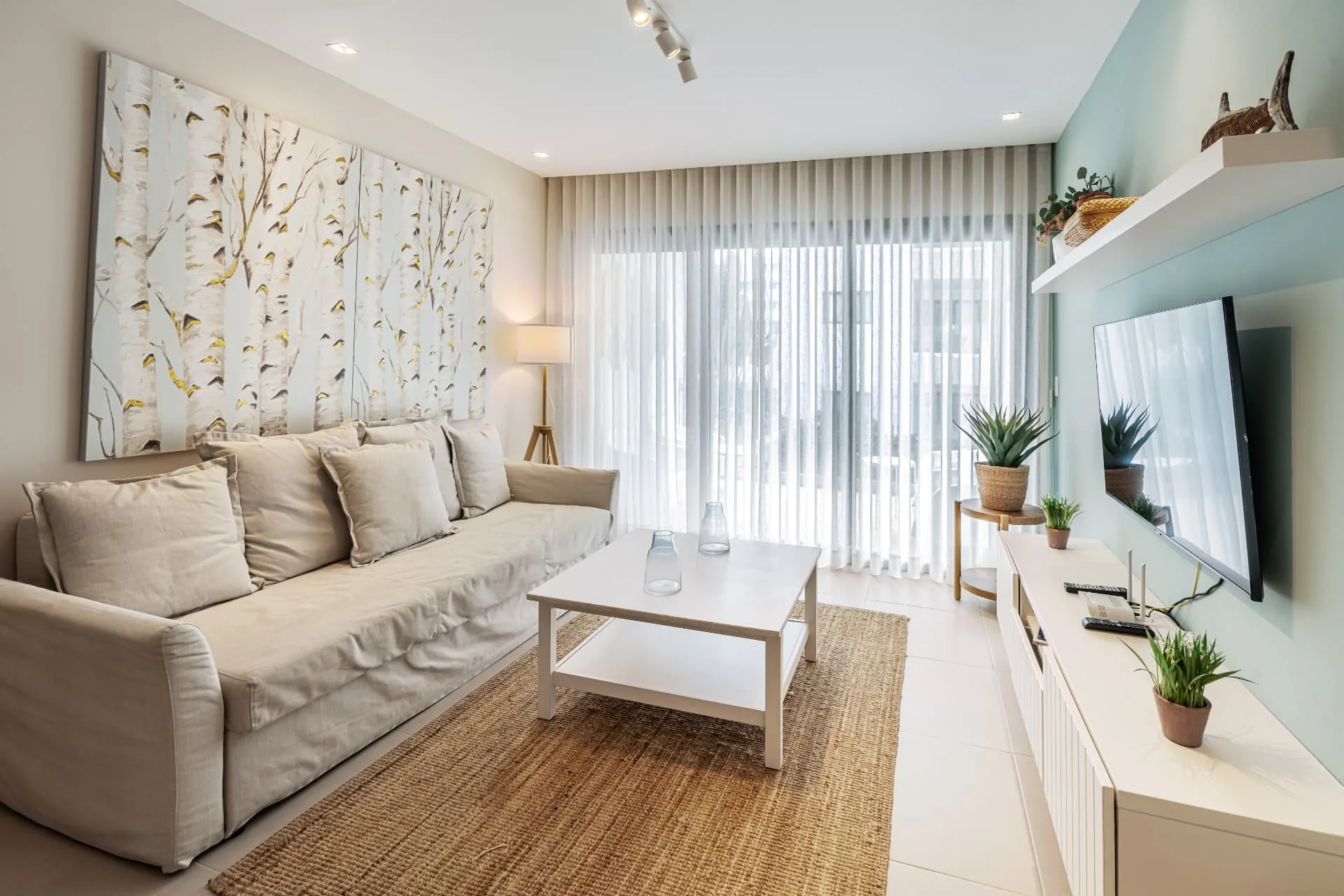 Coastal living room with linen sofa, jute rug, birch artwork and sea-green media wall
