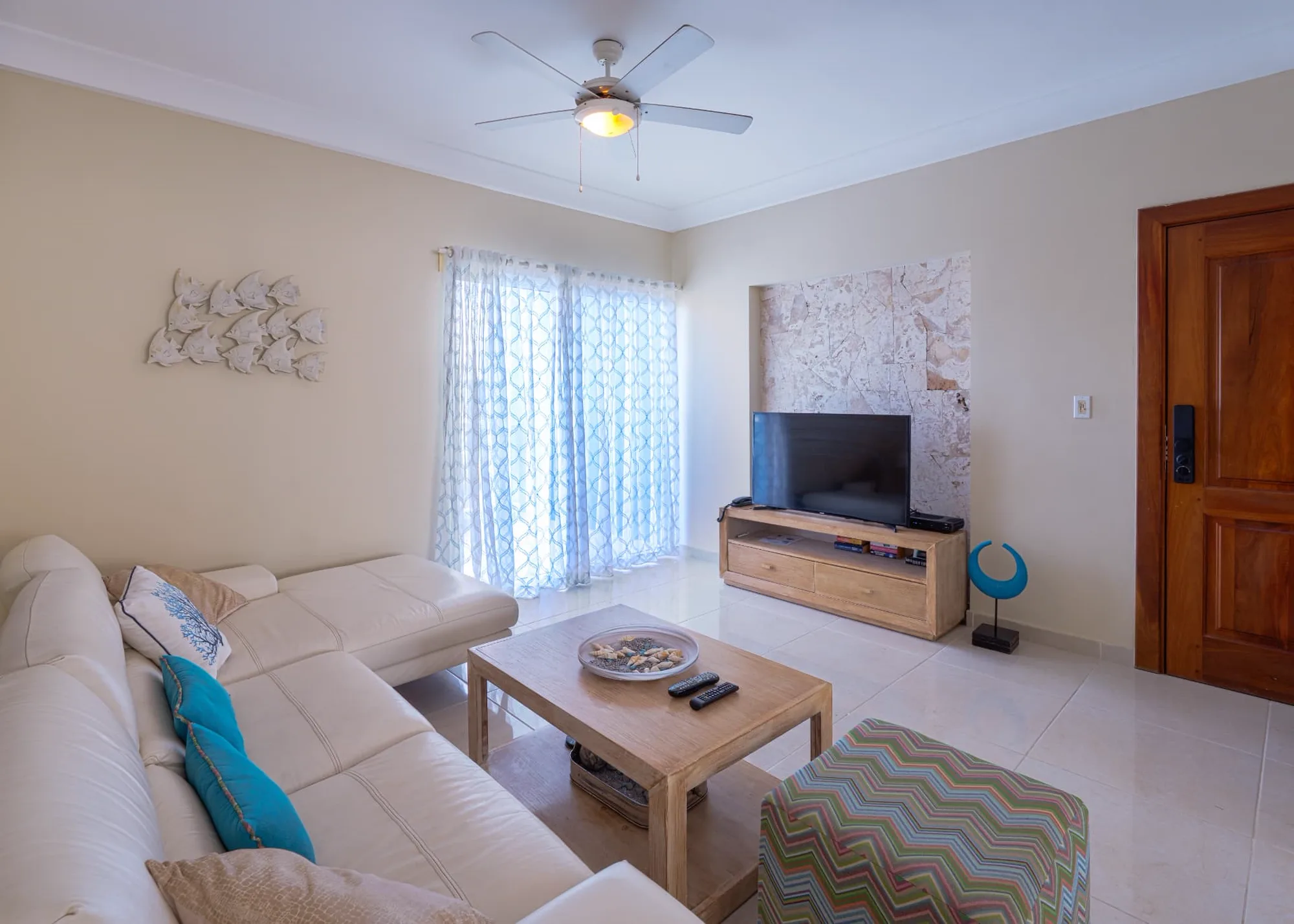 Living room looking toward the television on a coral stone feature wall with timber console and metal fish art