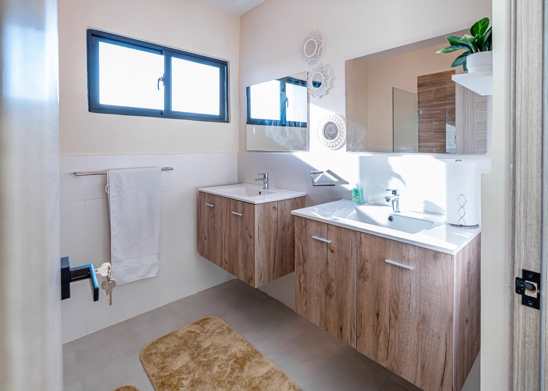 Primary bathroom with double floating mahogany vanities, twin mirrors and a glass walk-in shower