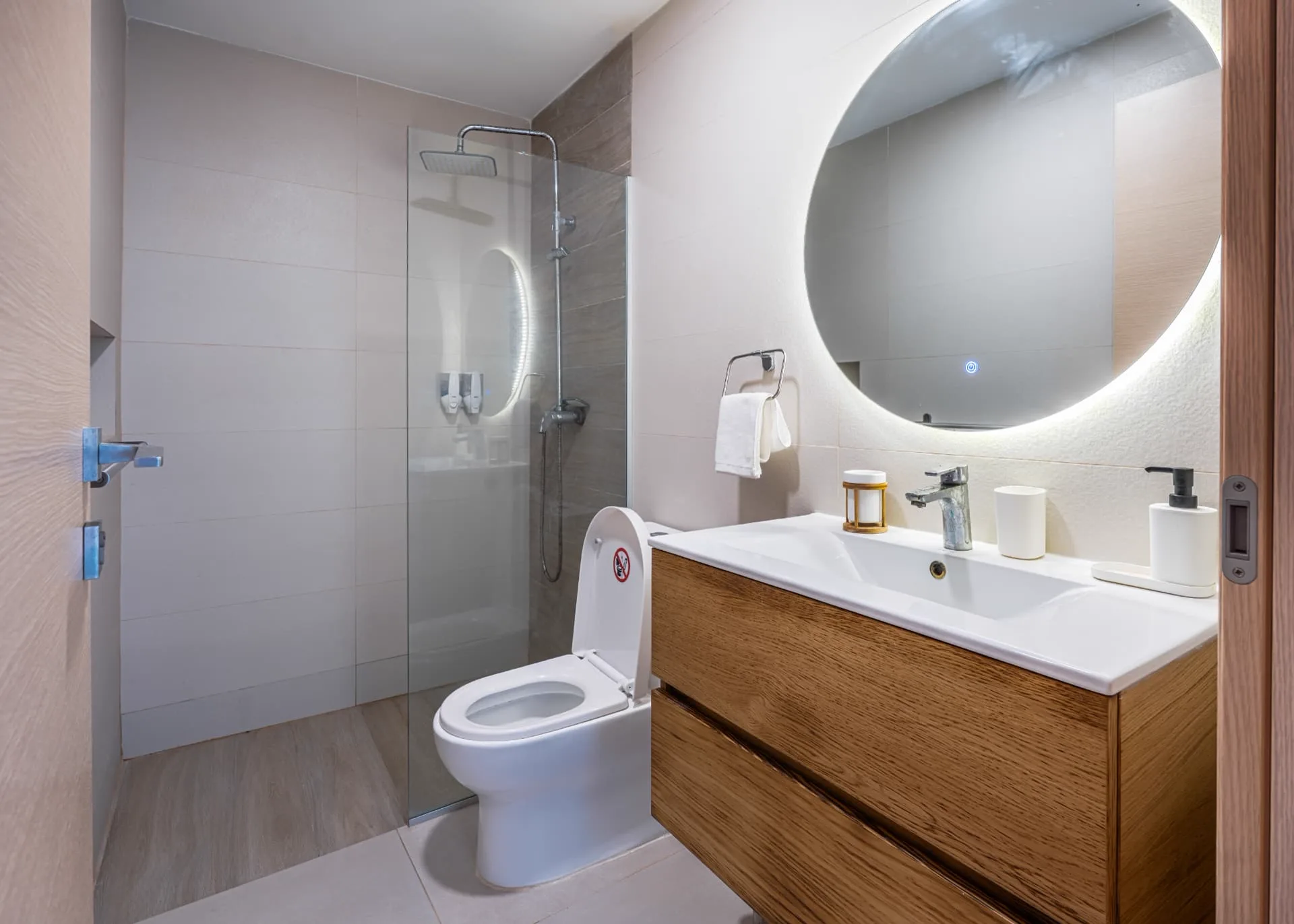 Bathroom with backlit round mirror, oak floating vanity and glass walk-in rain shower