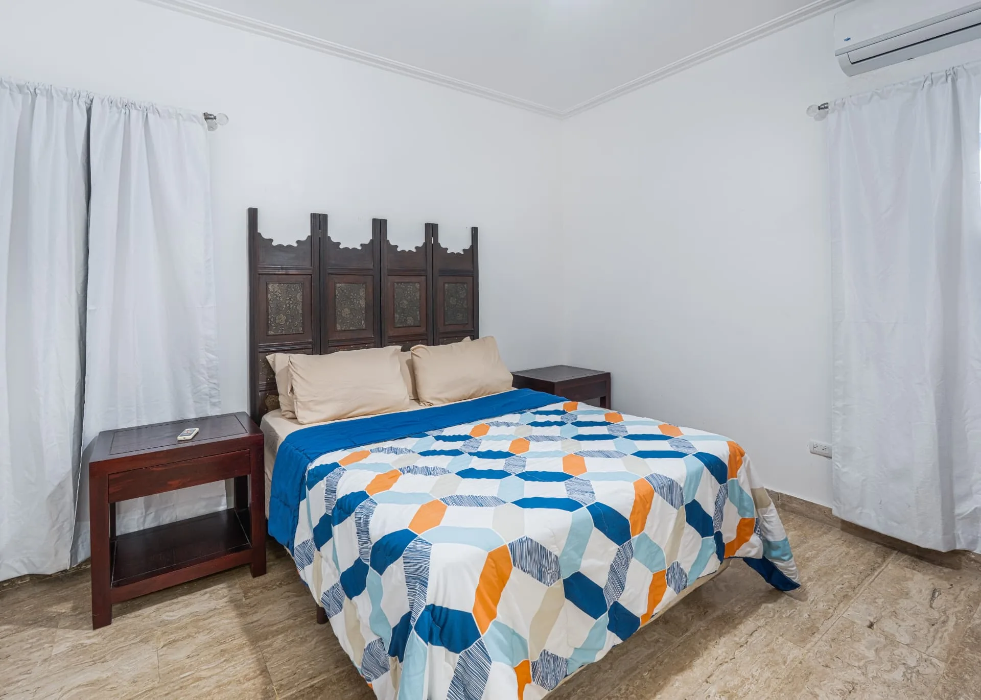 Bedroom with carved wood headboard, geometric bedding in blue and orange and matching mahogany nightstands