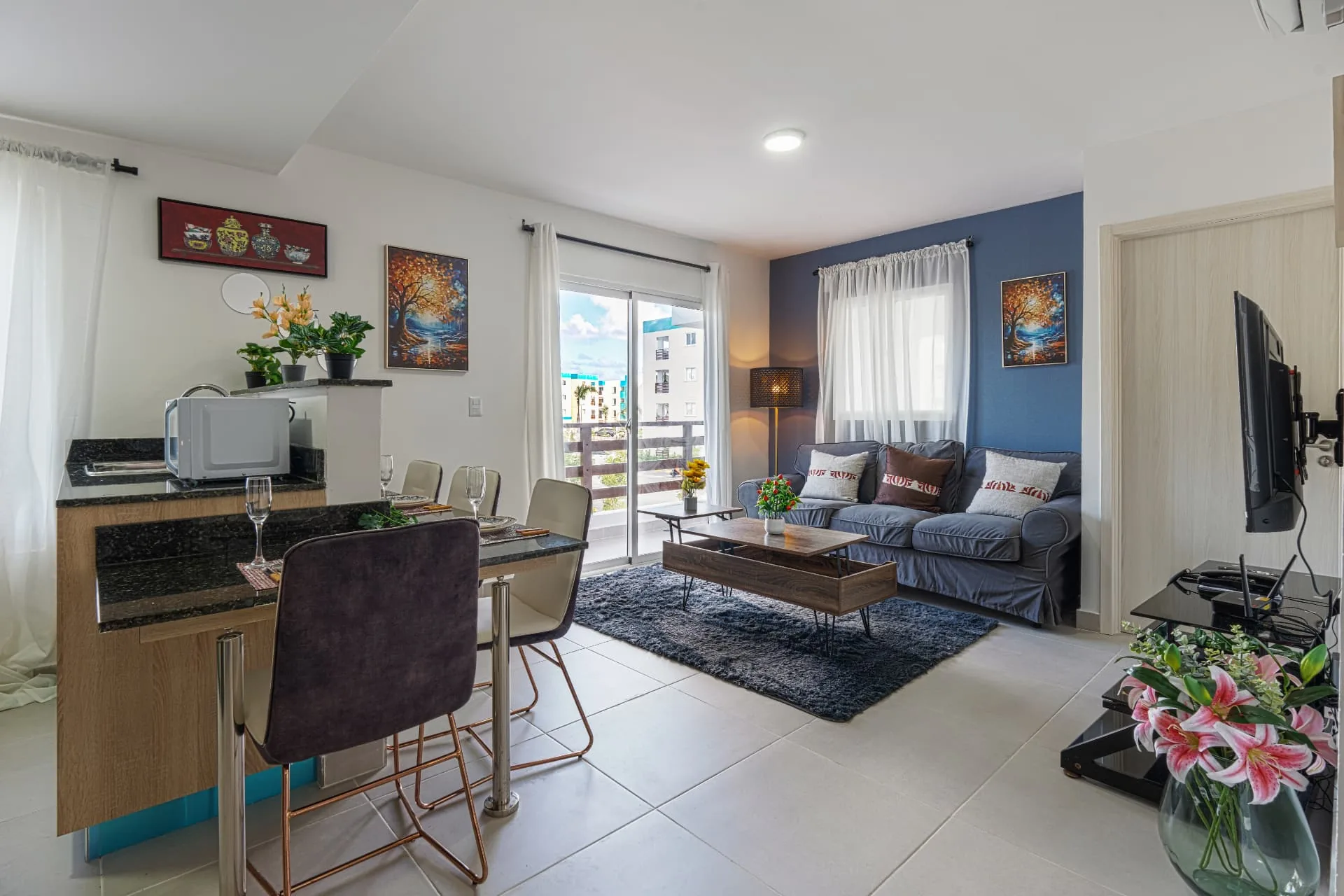 Open apartment living and dining area with breakfast bar, grey sofa and balcony doors