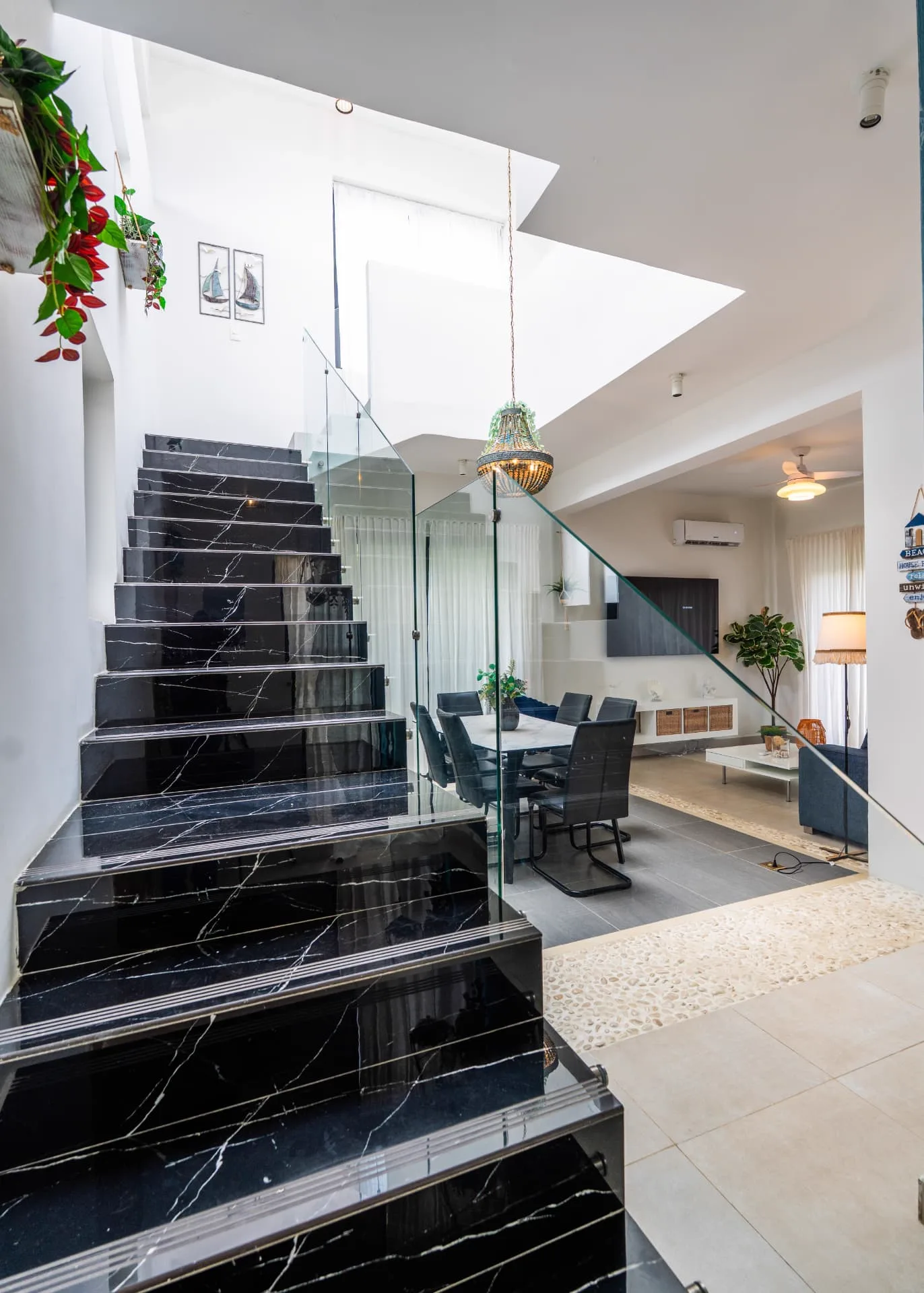 Entry hall with black marble staircase, glass balustrade and beaded chandelier over the dining table